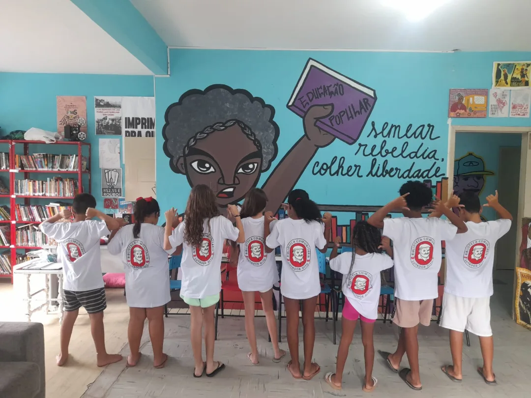 Crianças na Biblioteca Comunitária Lutador Dito diante de um mural de educação popular